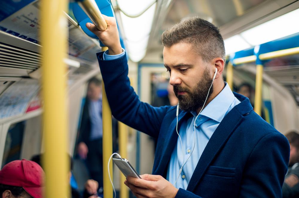 A professional using phone and headphones while standing inside a train
