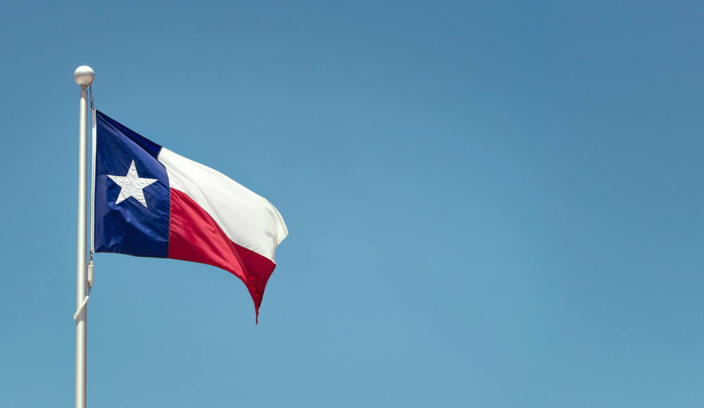 Texas State flag on the pole waving in the wing against bright blue sky